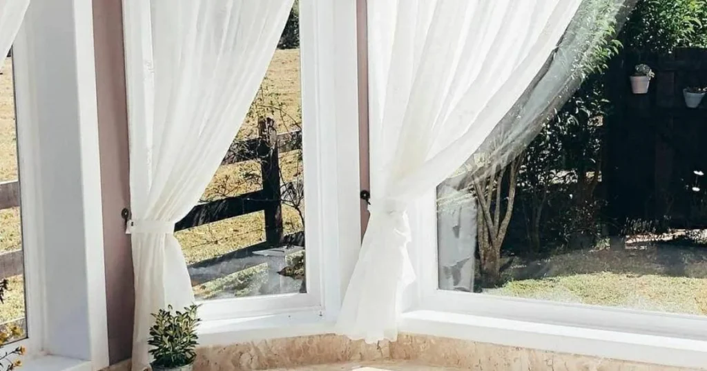 Cortinas brancas e luz natural em suíte da pousada.