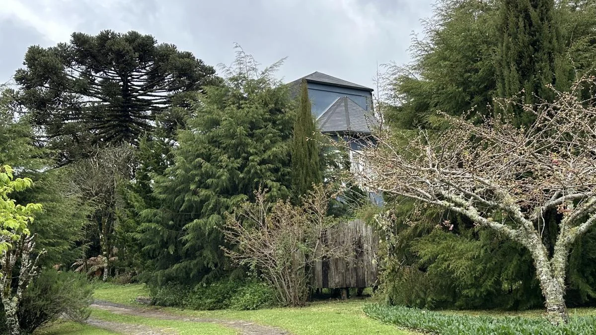 Vista externa do Sobrado Premium Amor Perfeito na Pousada Cantos e Encantos, cercado por árvores e jardim de altitude em Urubici, na Serra Catarinense.