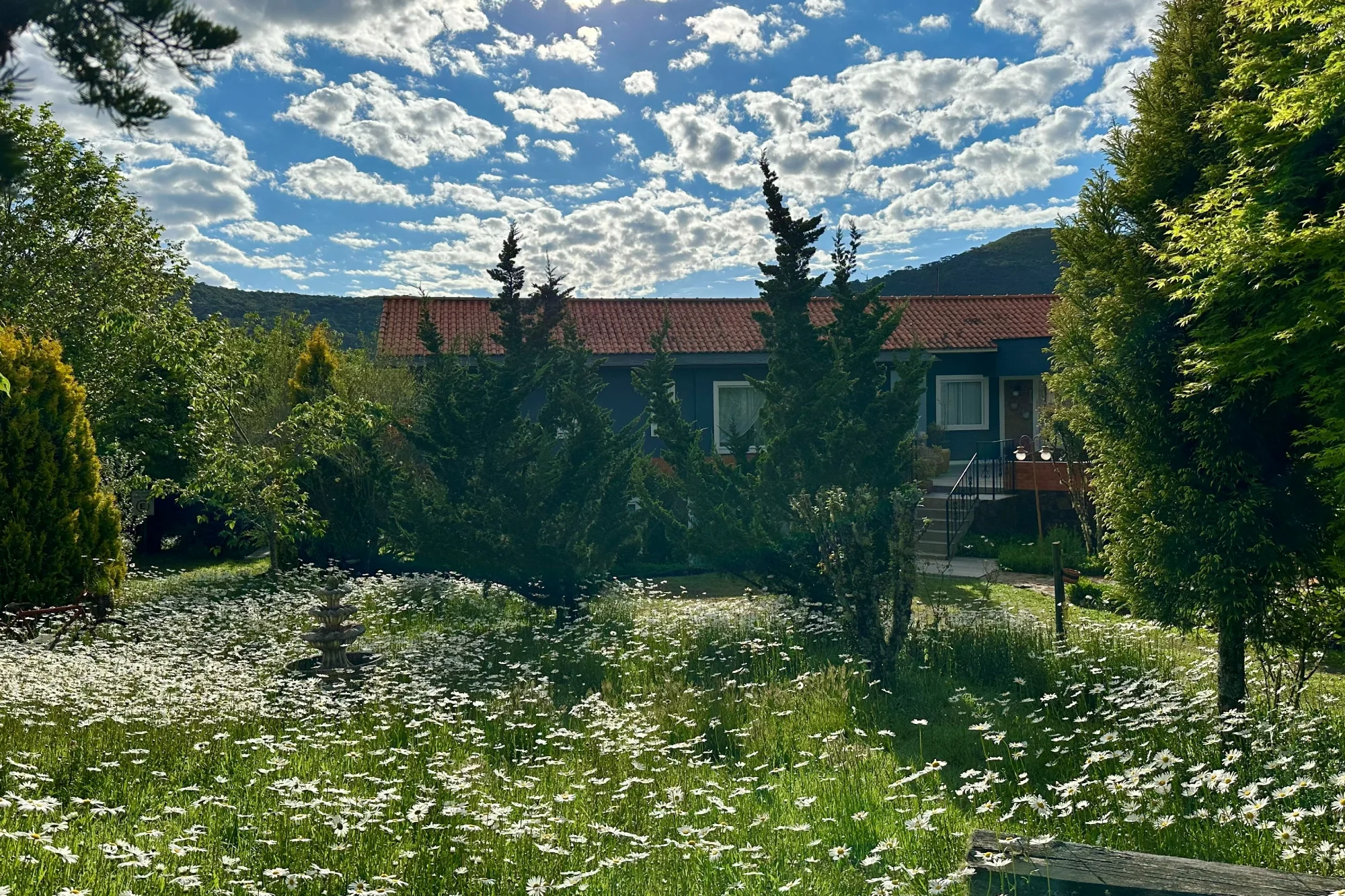 Jardim da Pousada Cantos e Encantos em Urubici, com flores silvestres, árvores e a pousada integrada à paisagem da Serra Catarinense